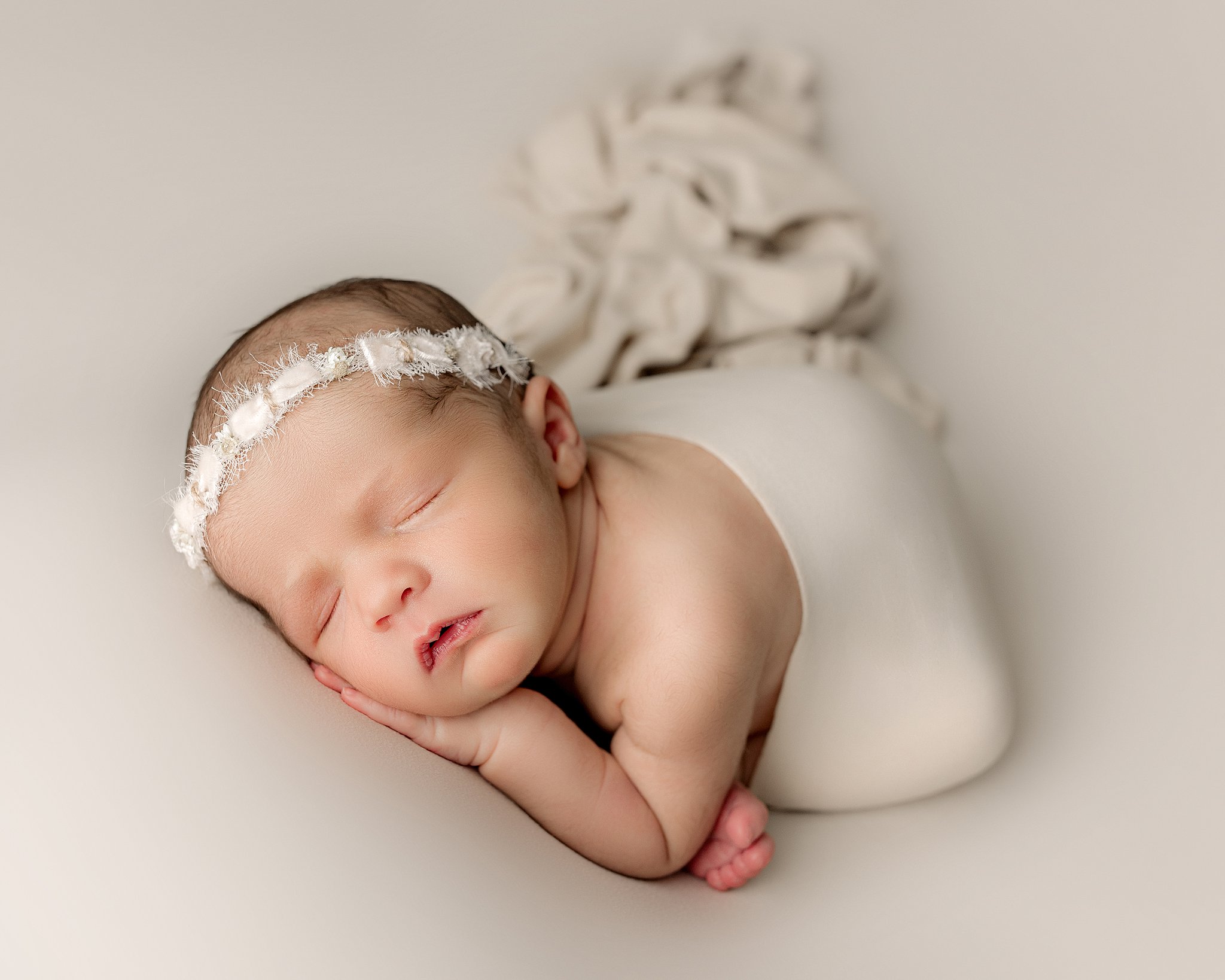 newborn baby in cream wrap and flower crown sleeping on her hands charleston baby boutique