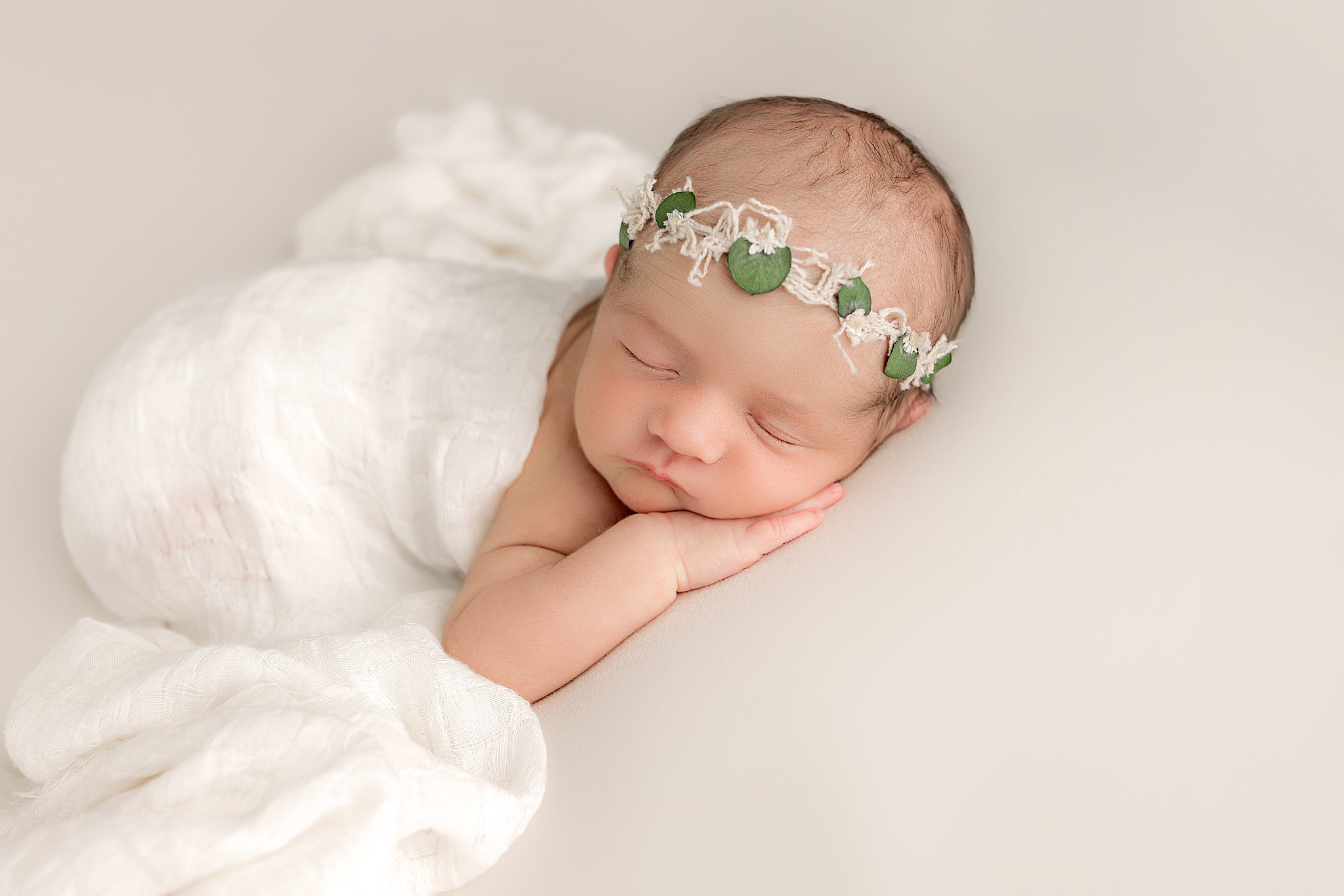 newborn baby girl in a white swaddle with a flower crown sleeping charleston baby boutique