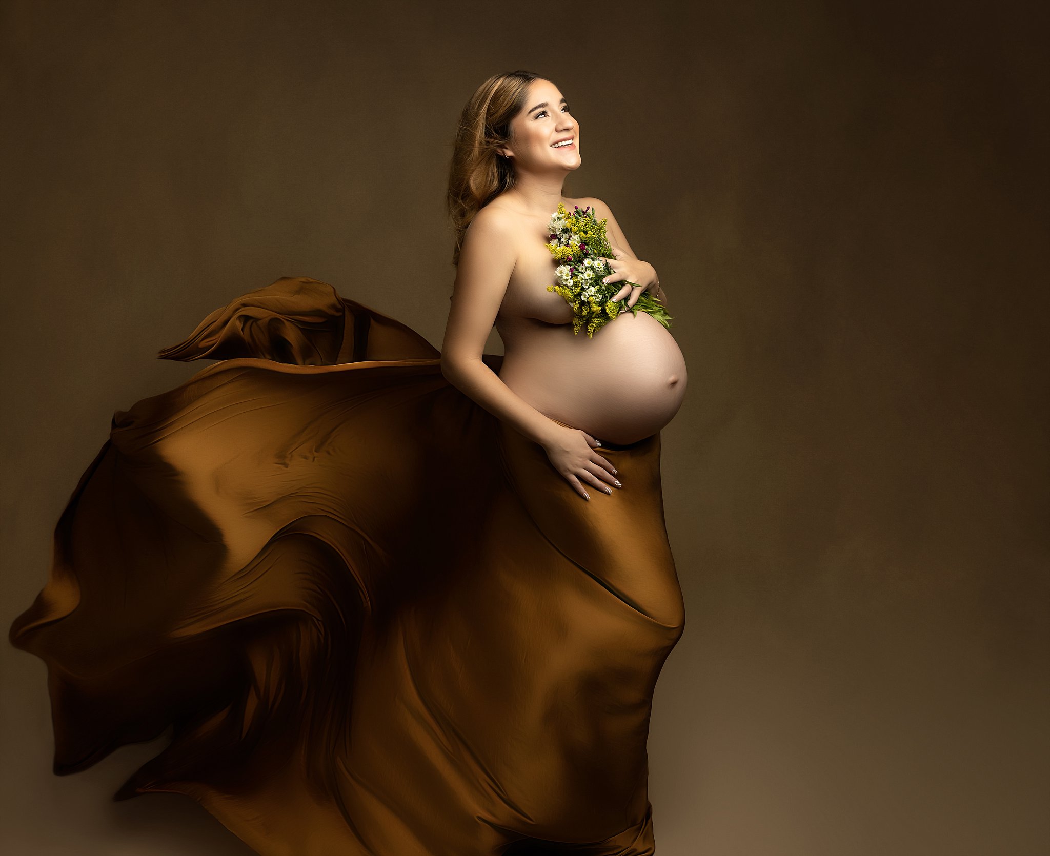 Mother to be stands in a studio with a long flowing gold dress