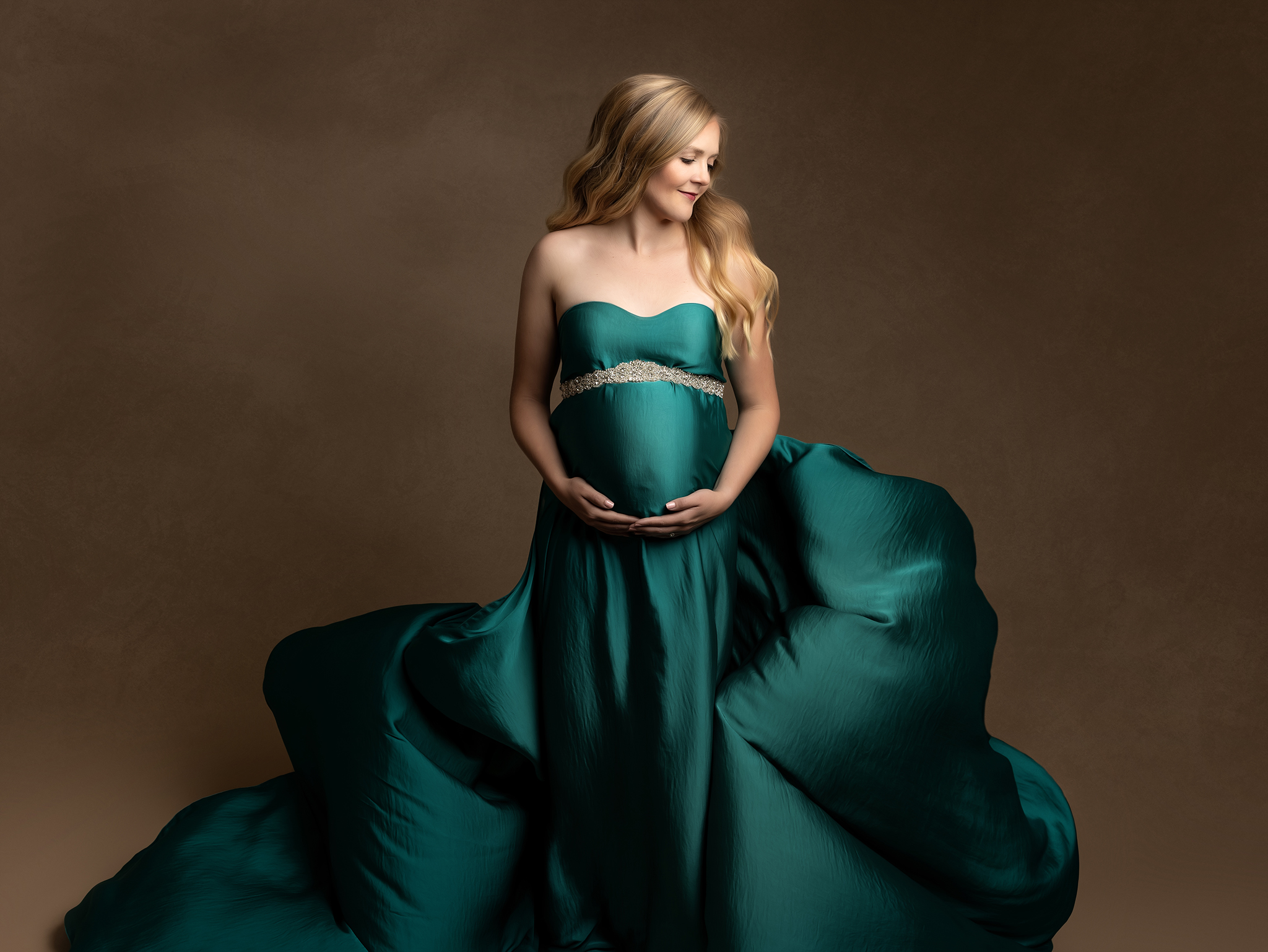 Pregnant woman stands in studio with a flowing blue maternity gown.