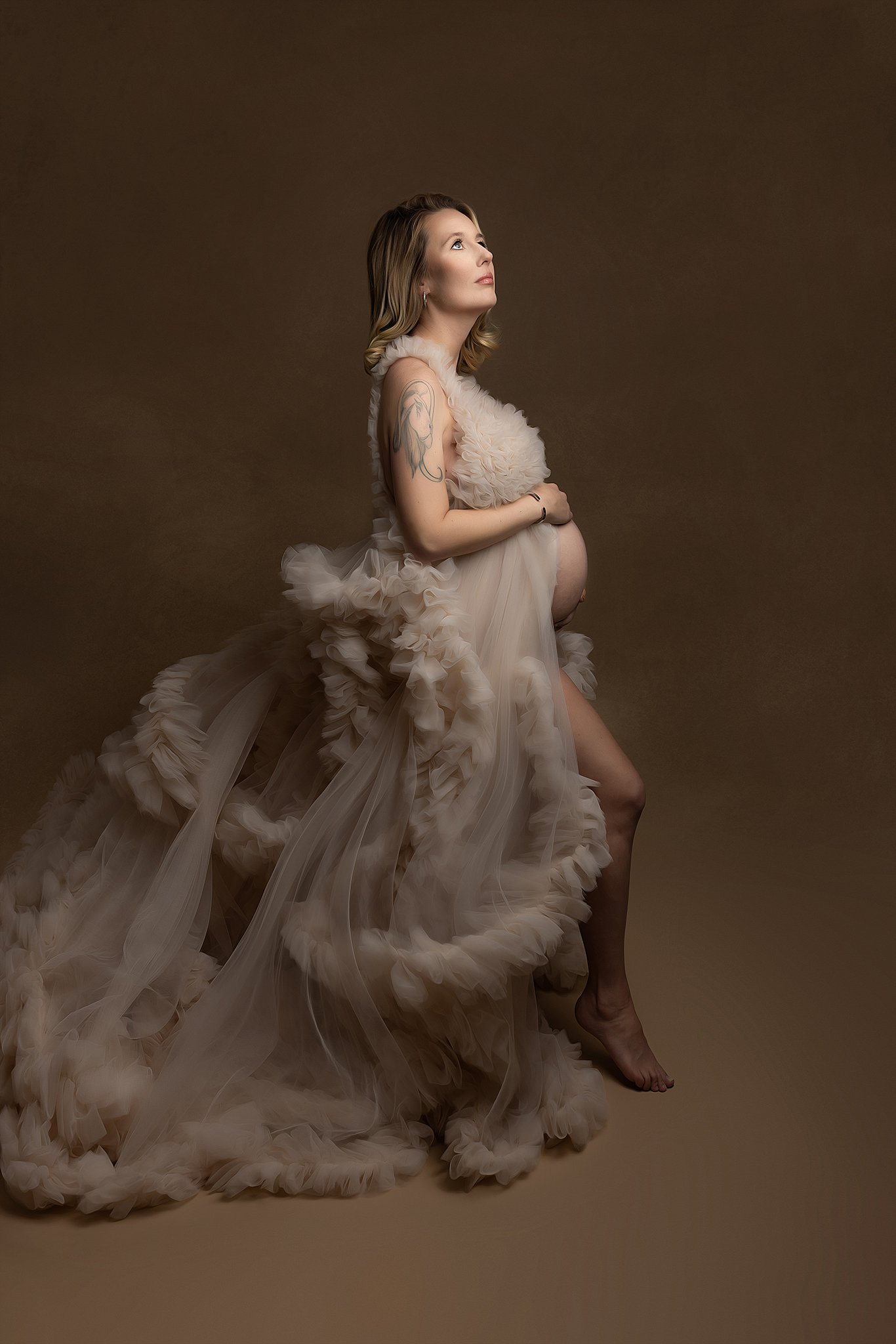 Mother to be stands in a studio in a flowing velour dress charleston doulas