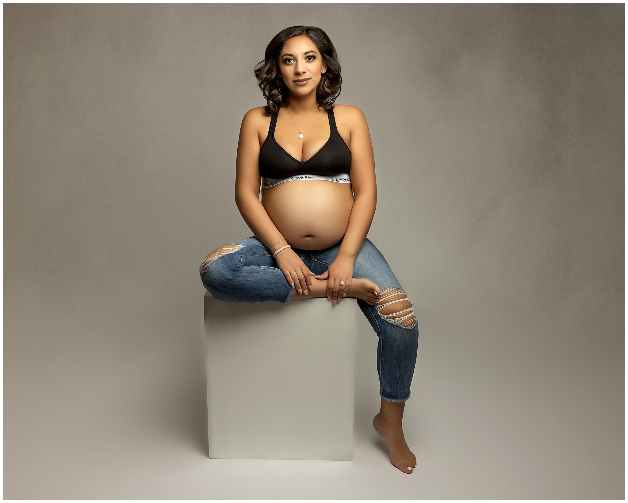 A mother to be sits on a grey box with bump exposed in a studio midwives charleston sc