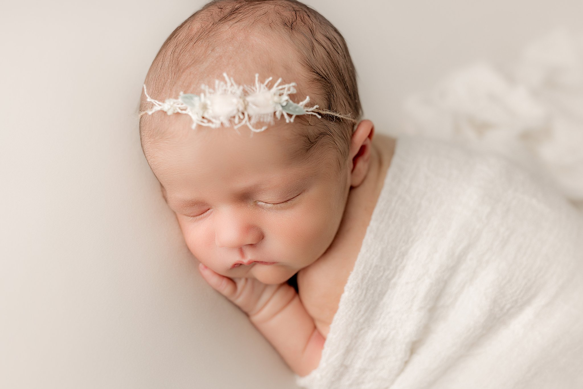 A newborn baby sleeps under a white blanket with a simple headband baby bloomers charleston