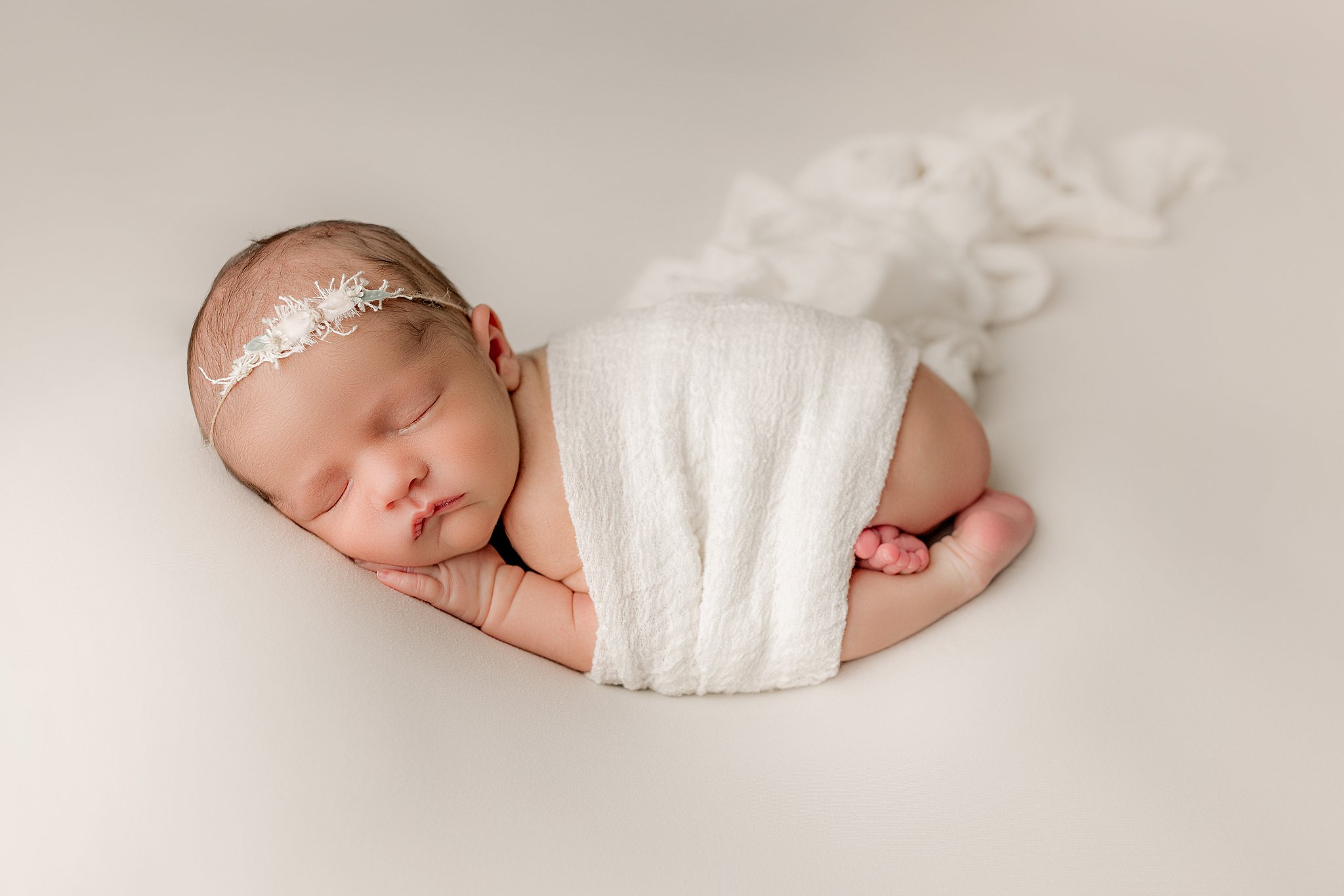 A newborn baby sleeps while wrapped in a white blanket in froggy pose ellifox