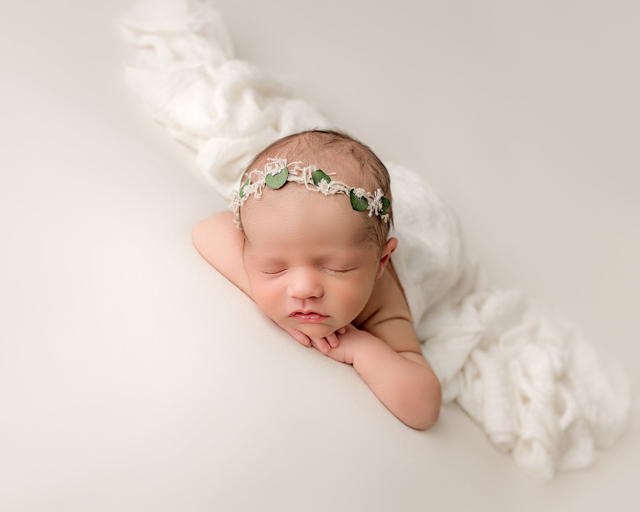 A newborn baby rests its head on its hands while sleeping on a white bed lowcountry baby boutique