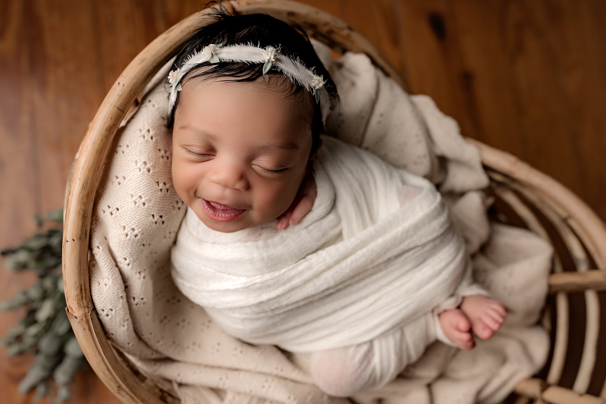 A smiling newborn baby sleeps in a wicker basket and white swaddle your happy nest